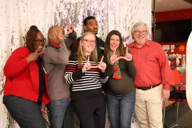 group of six people, the Student Affairs Leadership Team, stand close to each other with a sparkly backdrop and 