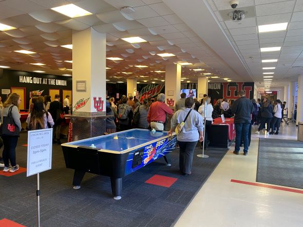 Large group of people stand among pool tables in the recreation area of the Union facing the television screens during Lori's keynote.