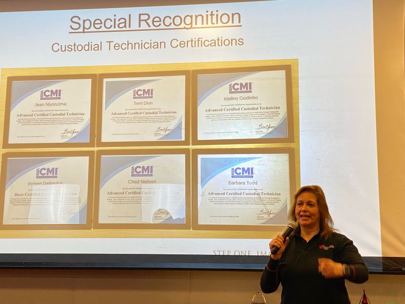 HRE staff memeber stands speaking into microphone with a slide behind her showing six Custodial Technician Certifications.