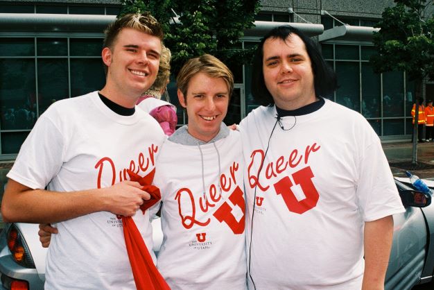 three people stand with arm around each other wearing "Queer U" T-shirts