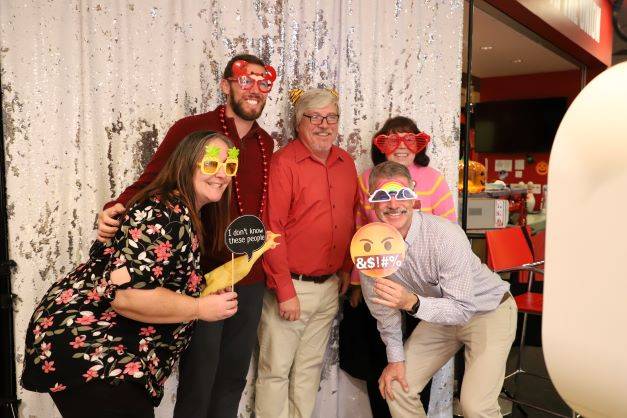 group of five people pose for photo in front of a sparkly background at a photo booth holding props.