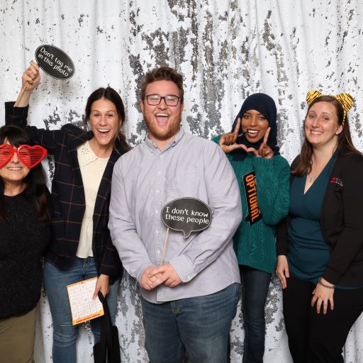 group of five people pose for photo in a photobooth with sparkly background. 